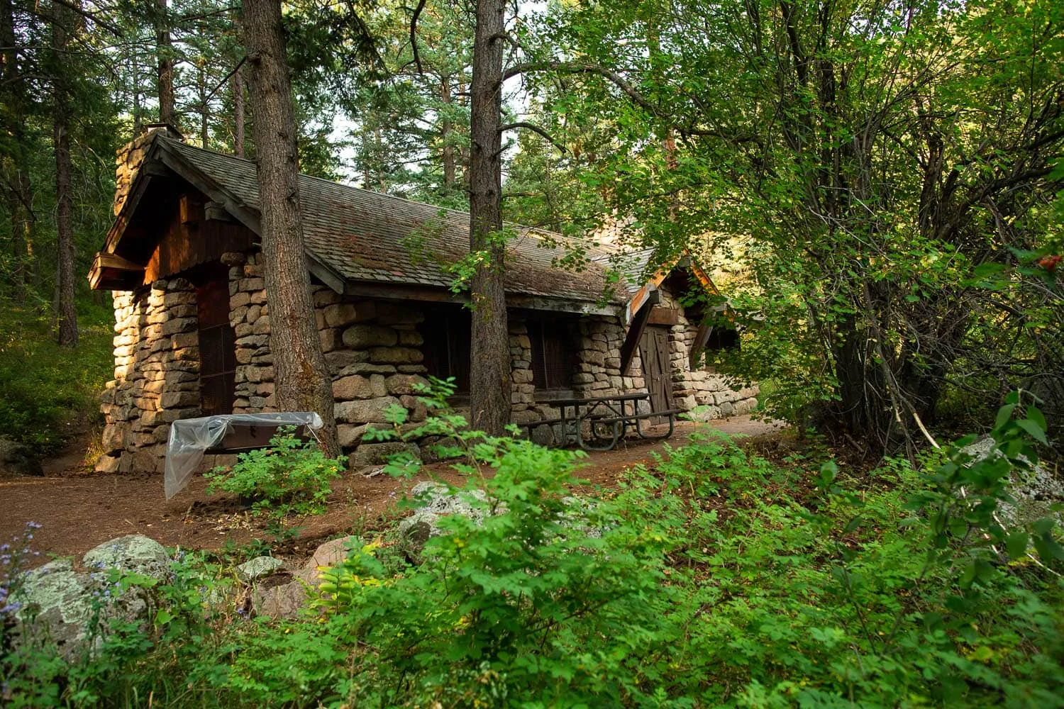A stone cabin is surrounded by green forest in the mountains of Colorado near Boulder.