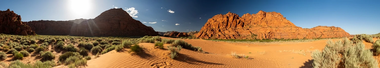 A panoramic image of the Snow Canyon state park dunefield with blue sky and orange sand.