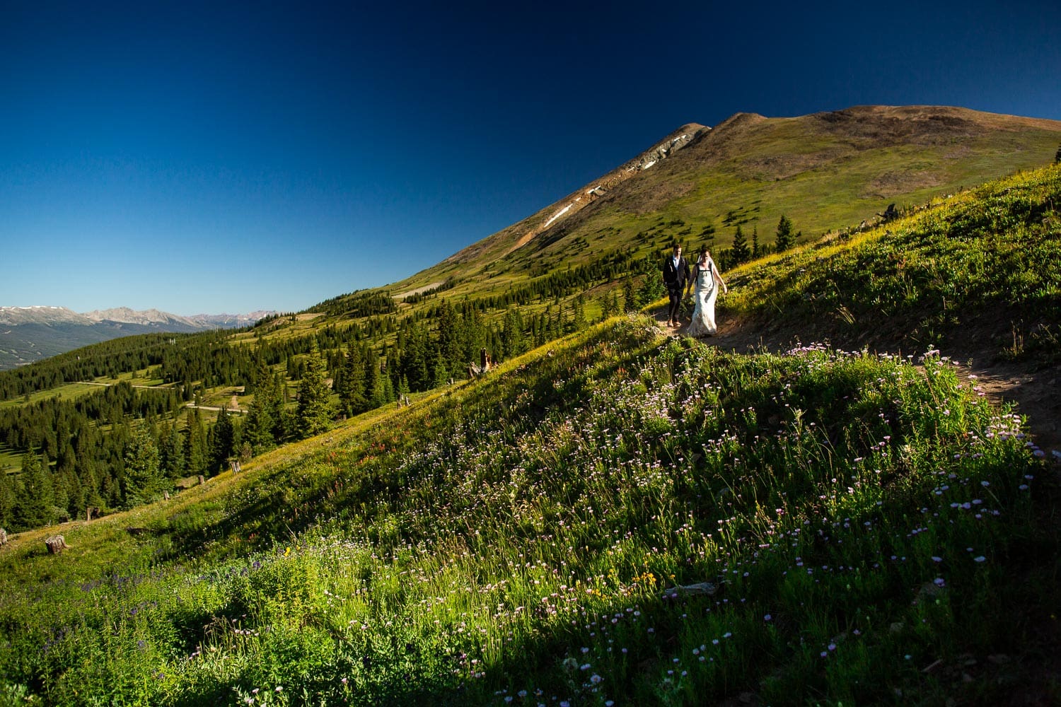A hiking elopement couple with backpacks takes a trail near Breckenridge, Colorado.