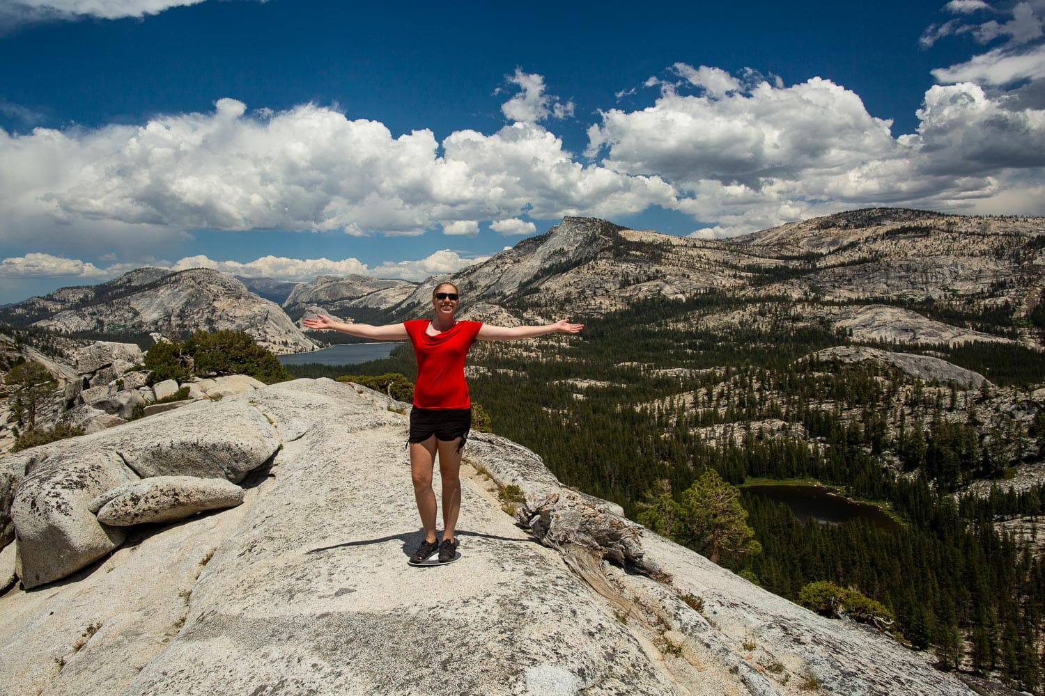 Yosemite elopement photographer Lucy Schultz stands in a red shirt with her arms out at a vista point.