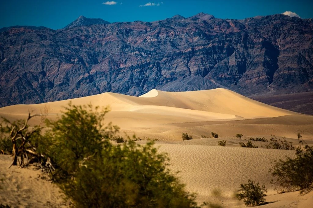 Sand dune peaks in Death Valley, California against jagged mountains.