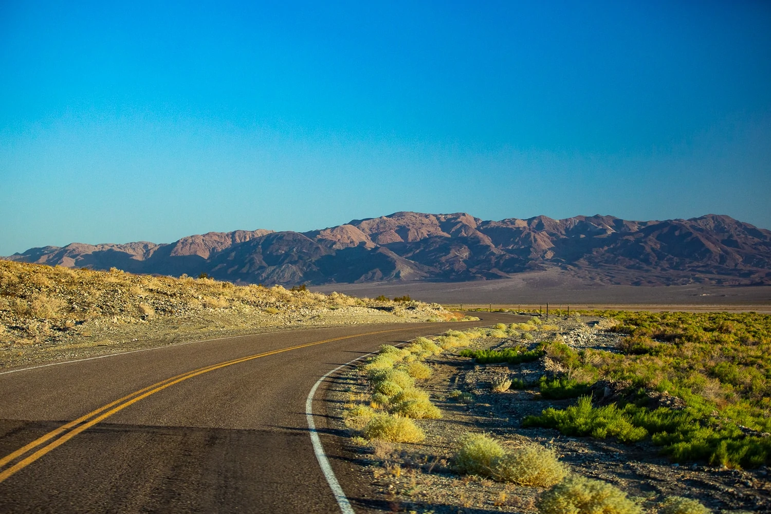 A road curves towards distant mountains in Death Valley National Park.