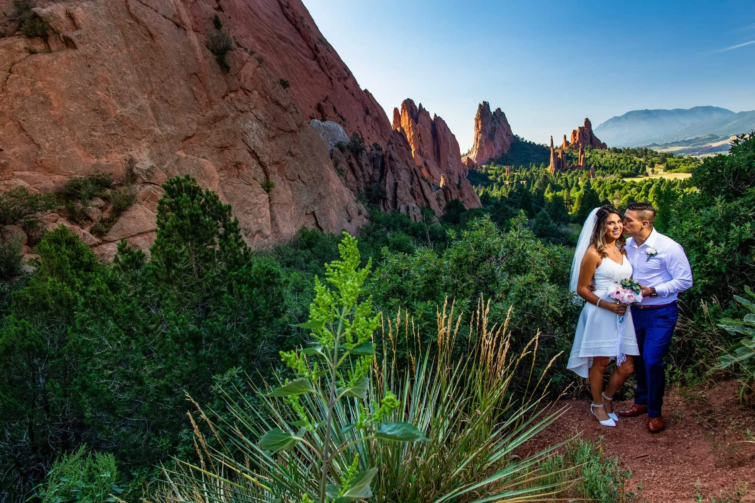 A hispanic groom kisses his new wife's cheek at Garden of the Gods