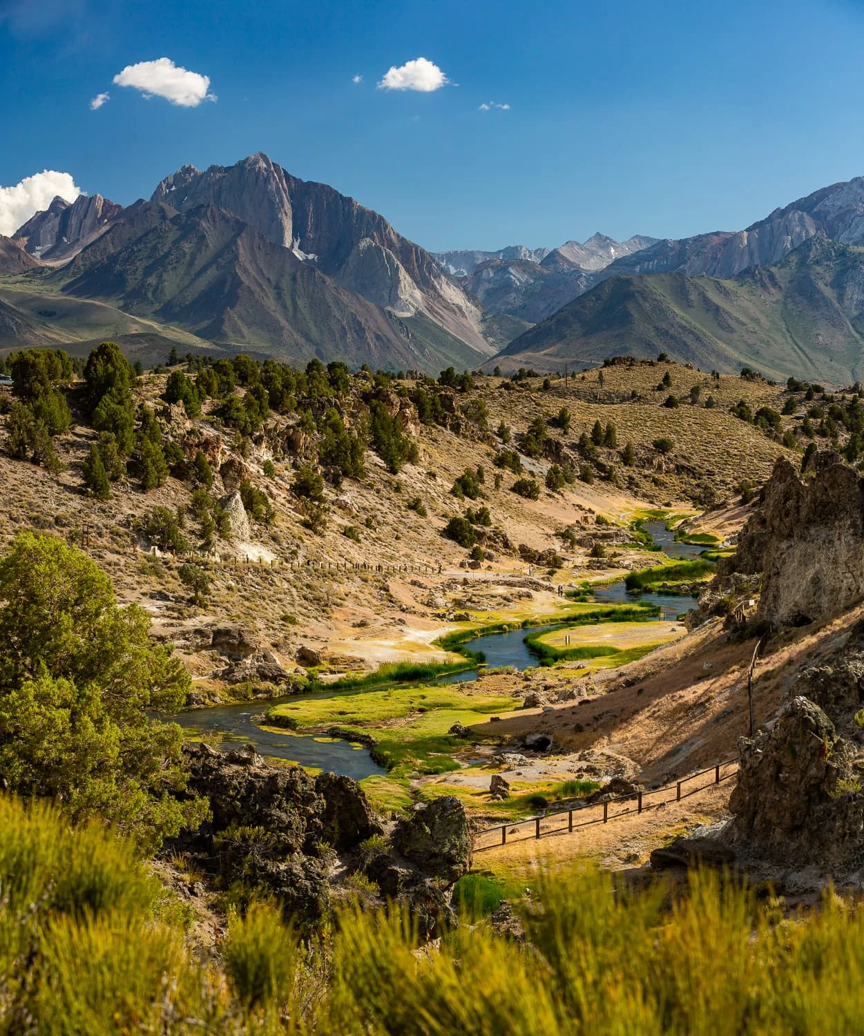 A colorful landscape photo looking west over the winding hot creek with mammoth mountain in the background.