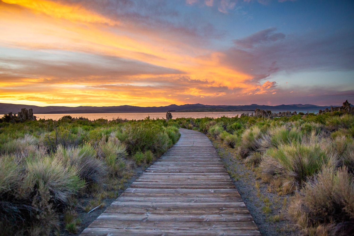 The wooden boardwalk leads to the shore of Mono Lake at sunset.
