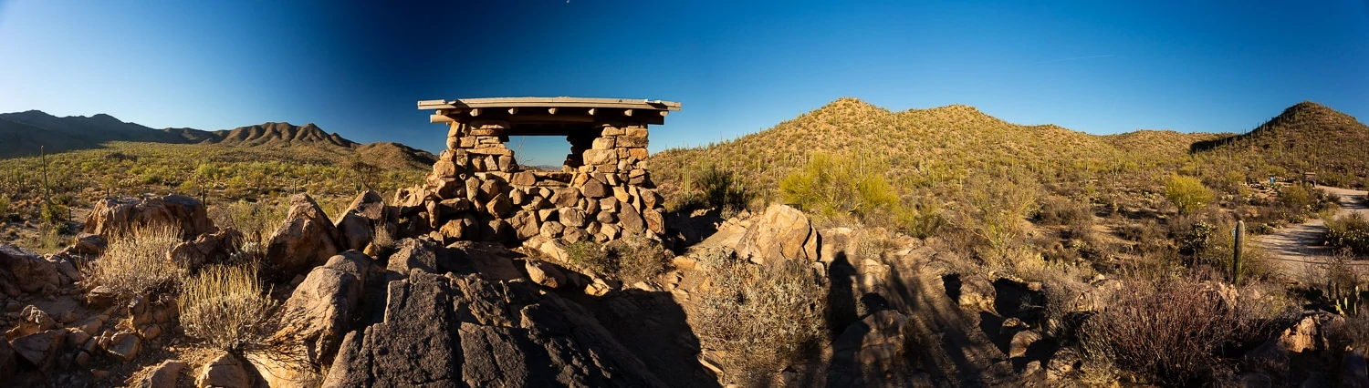 A small stone picnic structure atop a small hill in Saguaro national park looks out over a large area of saguaro cacti.