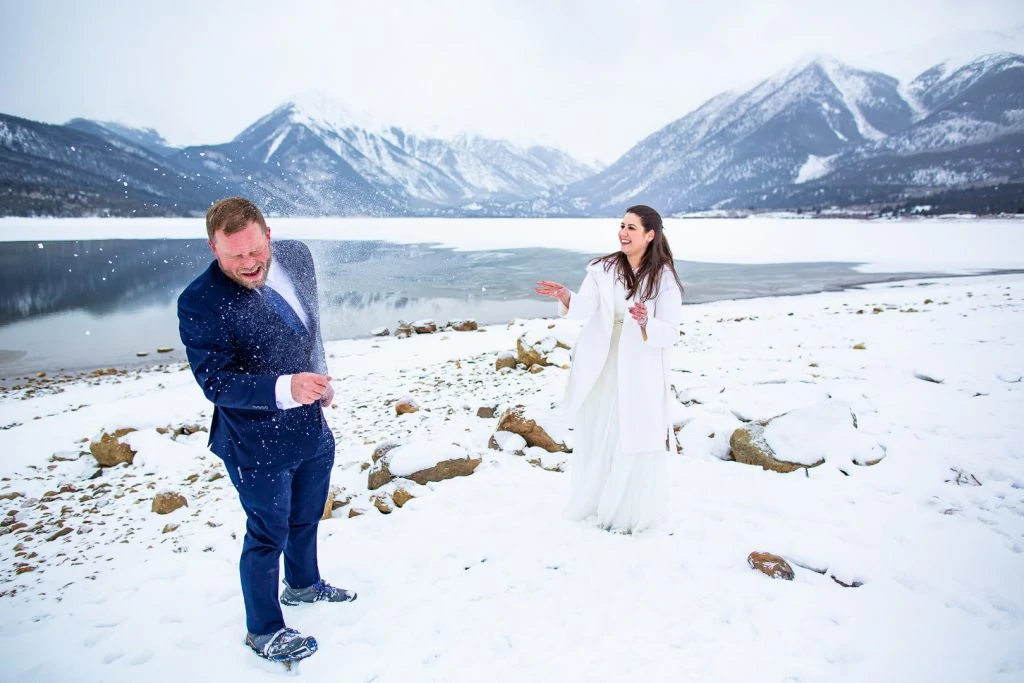 An elopement couple throws snowballs at each other.