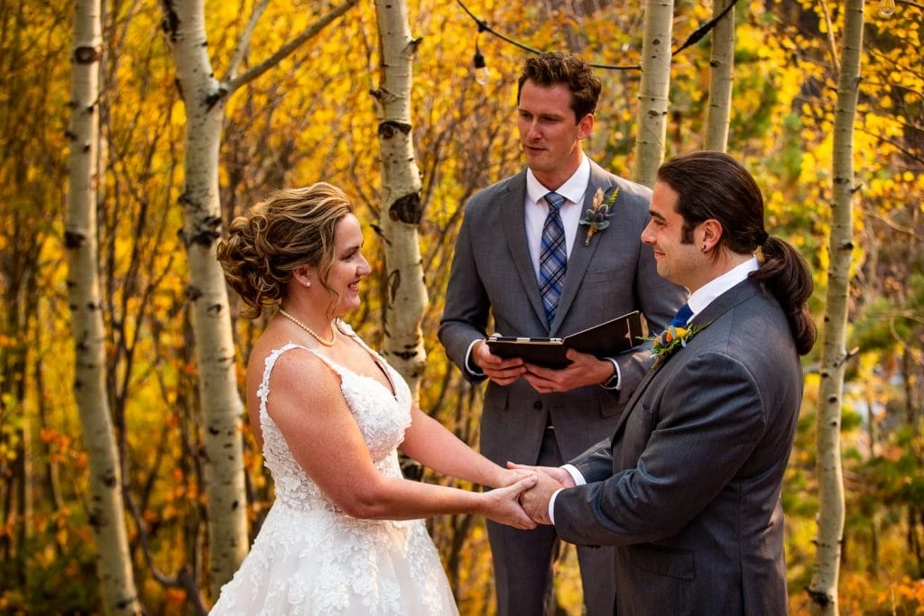 An elopement couple joins hands in an aspen grove as their officiant conducts the ceremony. 