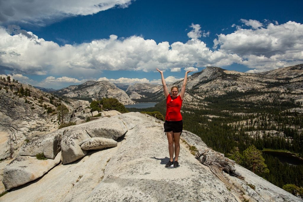 Elopement photographer Lucy Schultz raises her arms against the blue sky in Yosemite National Park in California.