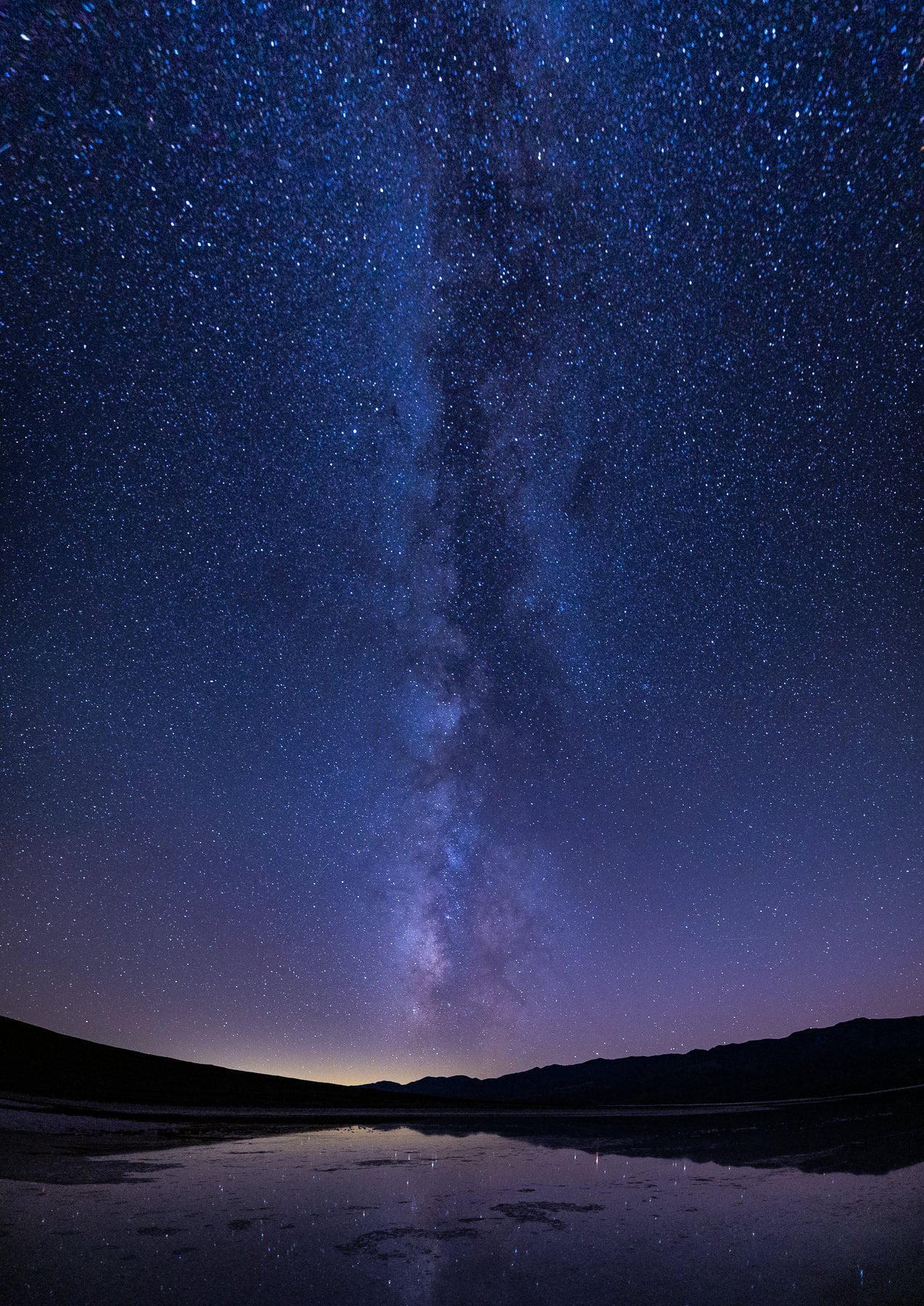 Death Valley's badwater Basin reflects the milky way against a purple sky in this astrophotography photograph.