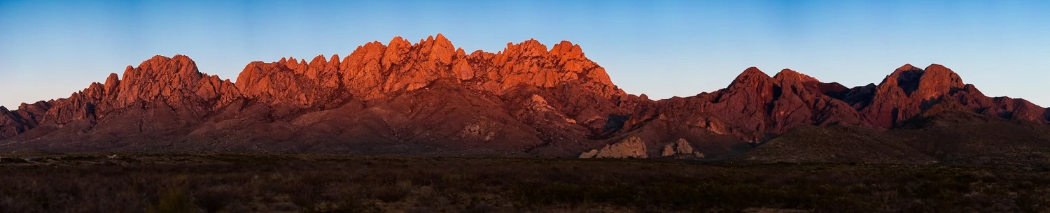 Sunset's warm glow covers the New Mexico mountains in an orange wash in this large panorama.