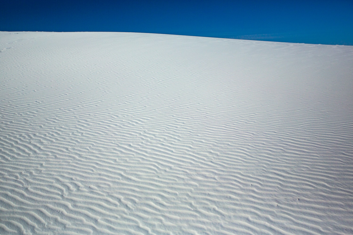 A view of a white sand dune against a blue sky backdrop at White Sands National Monument park.