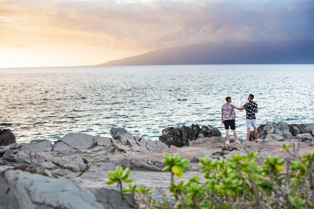A gay couple touches each other's shoulders on Maui's west side overlooking Molokai island at sunset.