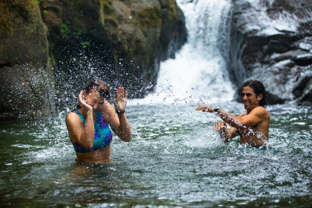 A man playfully splashes his wife at a waterfall in costa rica by underwater elopement photographer Lucy Schultz.
