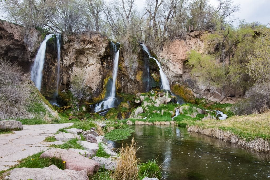 Three waterfalls tumble down a large cliff into a green grassy river in Rifle, Colorado.