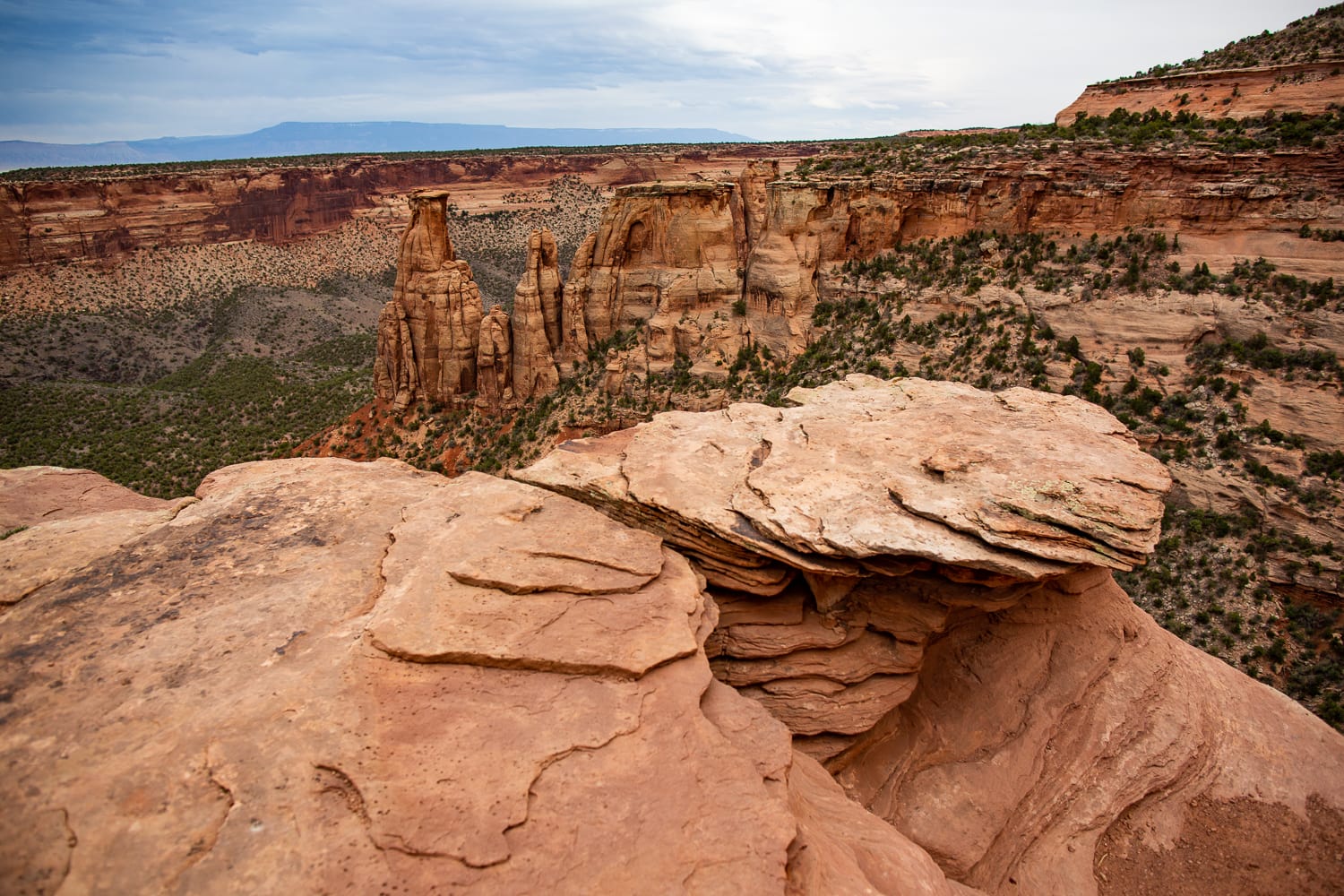 Layered reddish rocks in the foreground of a view of the dramatic Colorado National Monument canyon.