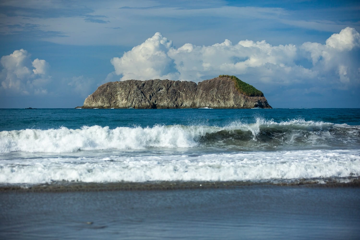 A large offshore rock is visible from the beach in Quepos, Costa Rica.