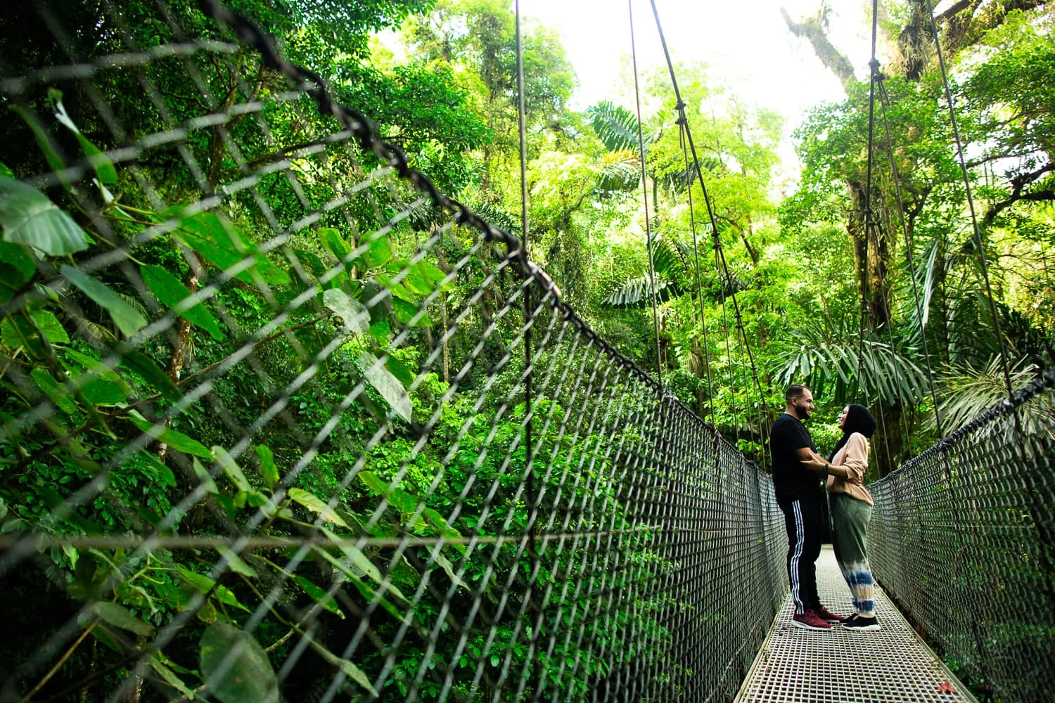 A woman wearing hijab embraces her husband on a swing bridge in the jungles of Costa Rica.