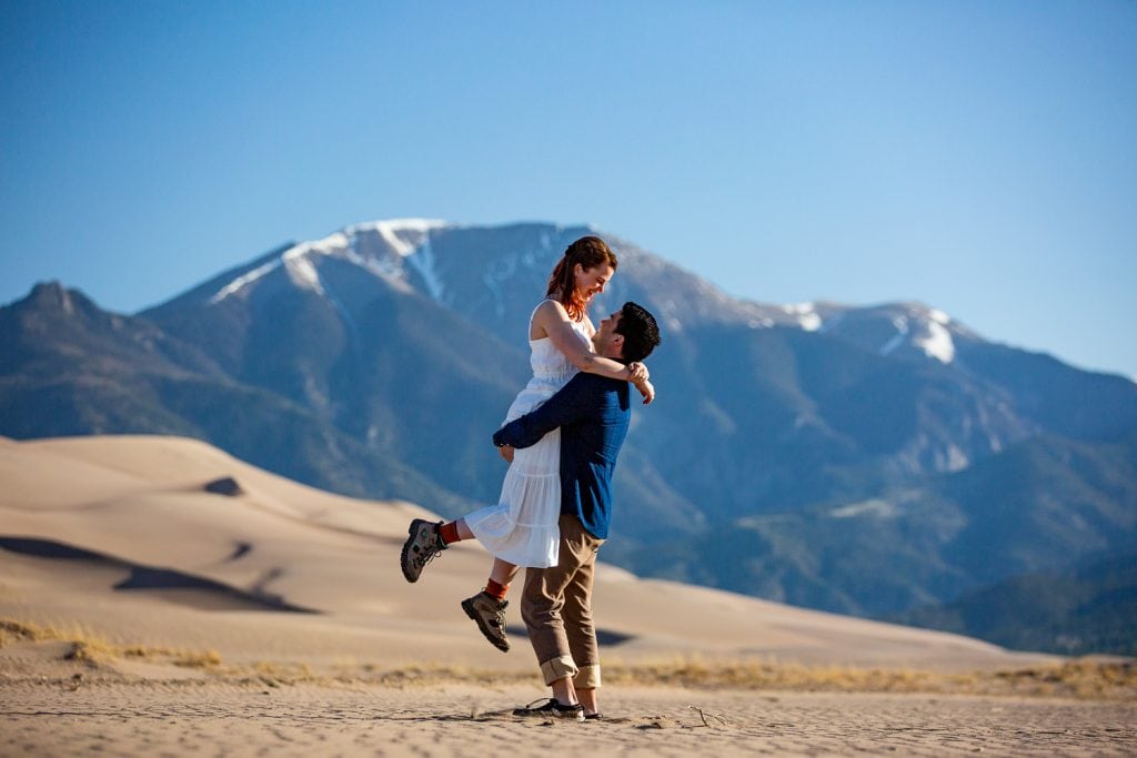 A groom lifts his bride wearing hiking boots at the Great Sand Dunes in Colorado.