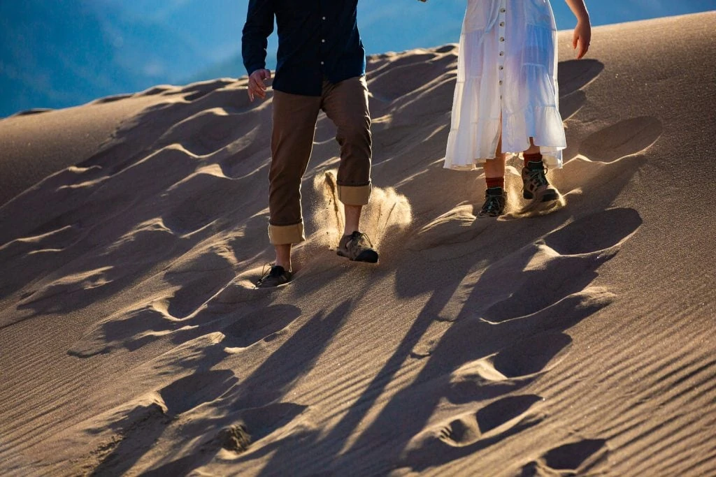 Sand flies behind an elopement couple's feet as they run down a sand dune.