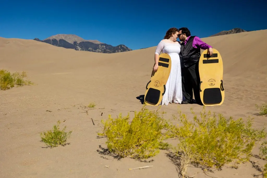 An elopement couple poses with their sand boards at great sand dunes national park.