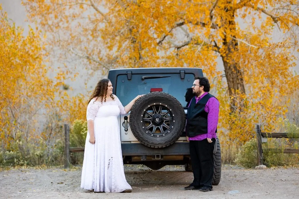 A wedding couple stands at the back of their jeep.