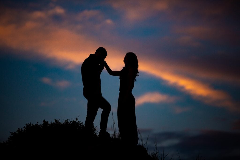 A silhouette of a man kissing his fiancee at sunset.