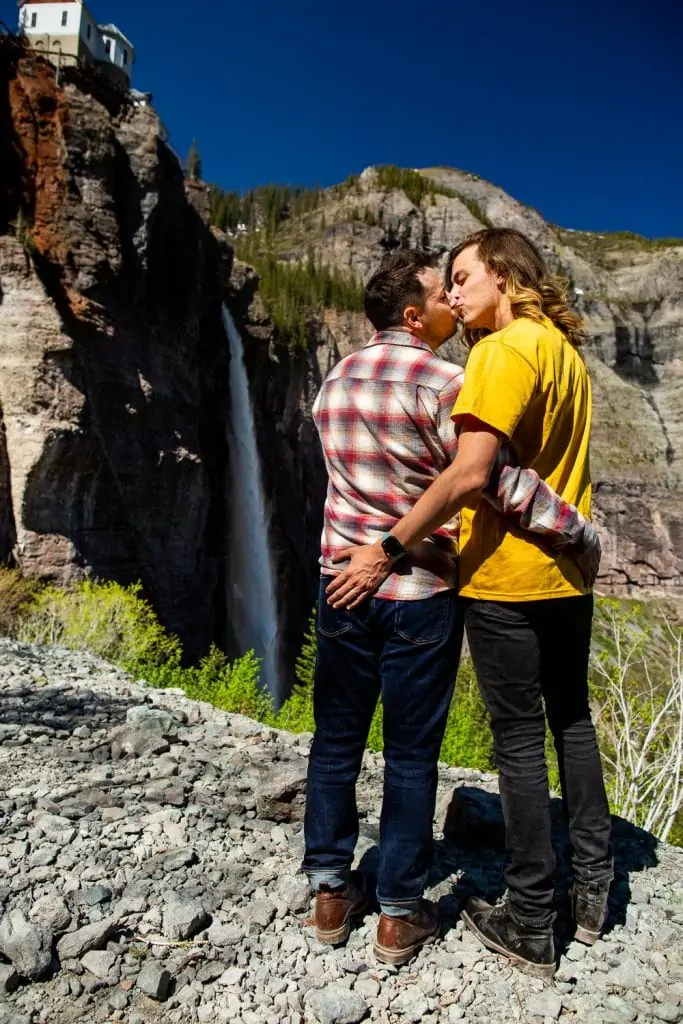 Two men kiss in front of Bridal Veil falls in telluride, Colorado.