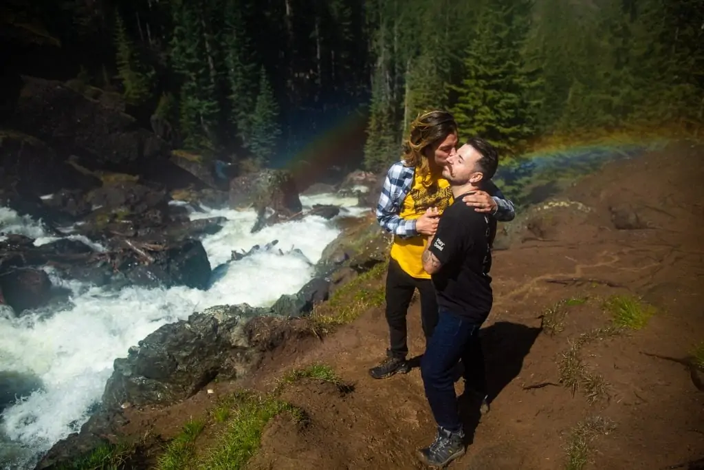 two rainbows surround two men at their engagement photo session at a waterfall.