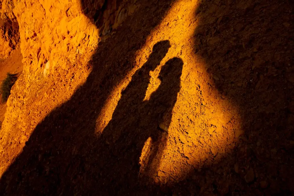 The shadows of a couple silhouetted in an orange rock.