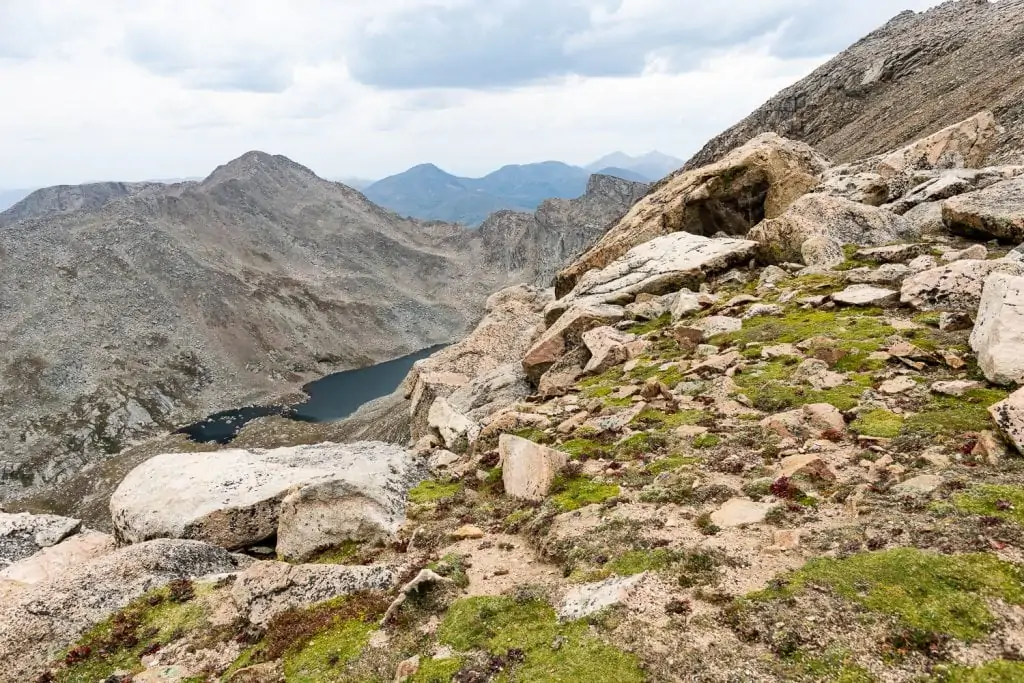 A stunning view of Mount Evans, with green vegetation, sand-colored rocks, blue water and bright sky, as one of the locations you can elope guided by Lucy Schultz Photography.