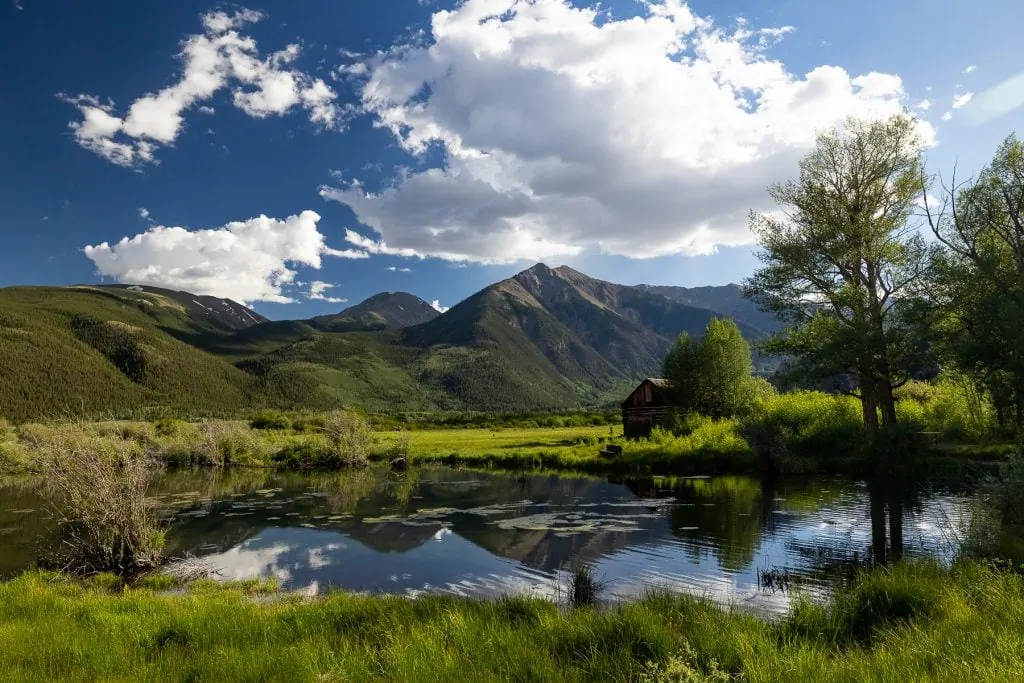 Twin Lakes in Colorado reflects the tall peaks of the area as a historic barn perches on the edge of the green grass.