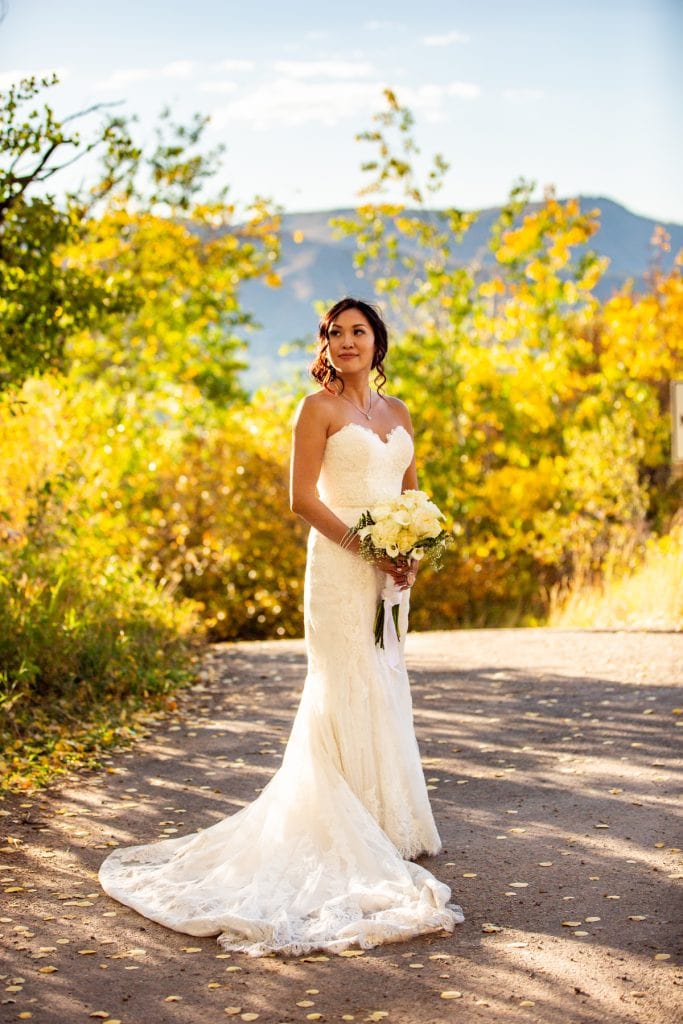 An asian bride wearing a strapless dress stands in front of fall foliage in Aspen, Colorado.
