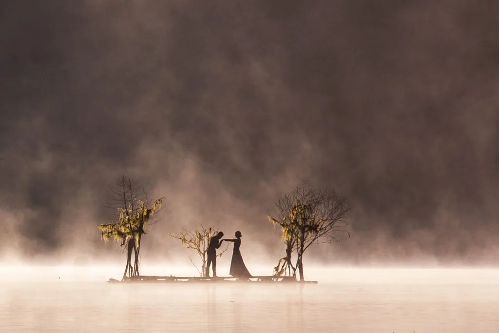 An elopement couple is silhouetted on a floating dock on a lake at sunrise in Bali.