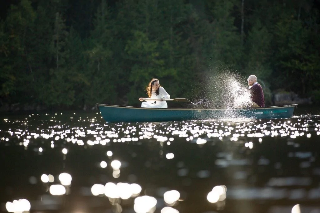 An elopement couple splashes each other in a canoe.