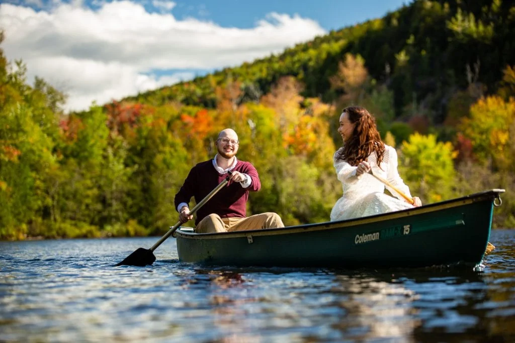 A couple in a canoe paddles across a lake with fall colors.