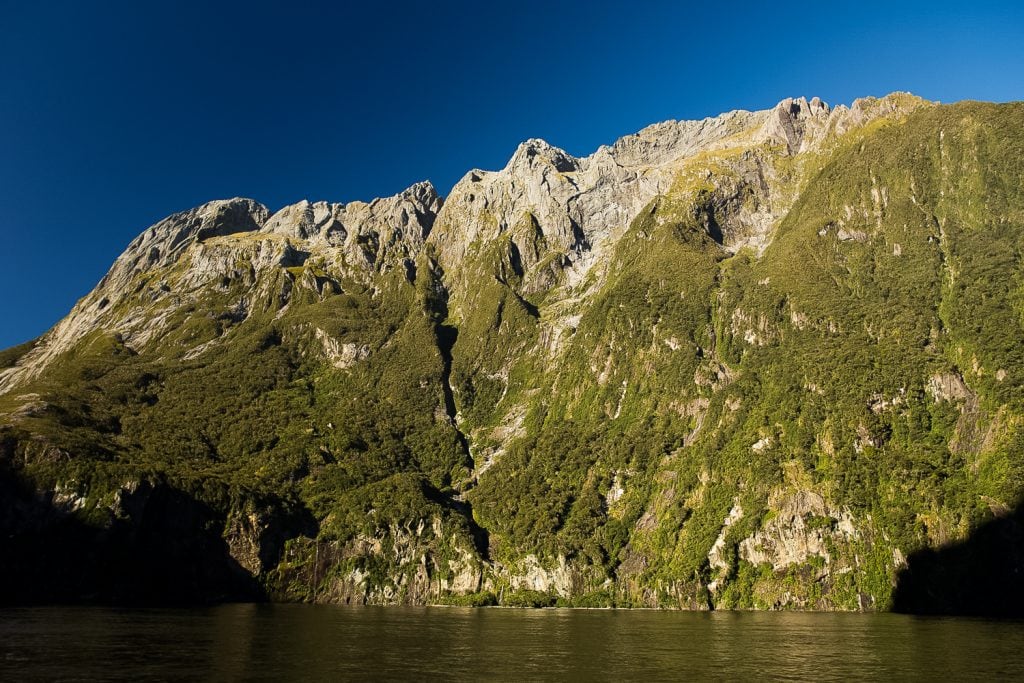 A towering mountain range with mossy sides at the edge of the ocean.