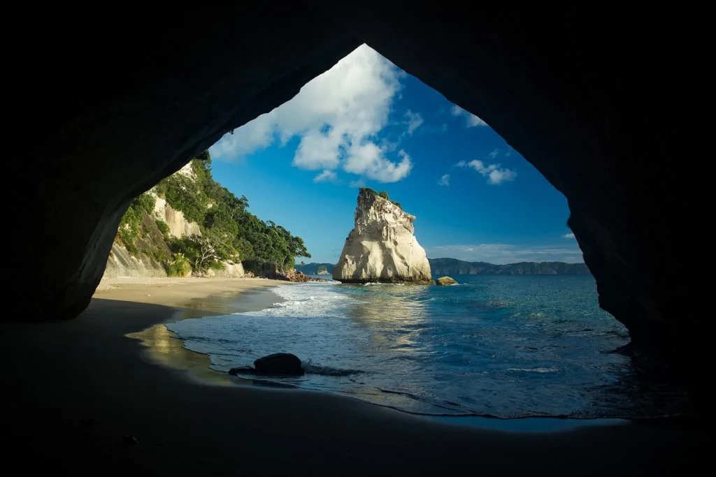 A rock overhang frames an offshore rock formation at Cathedral Cove, New Zealand.