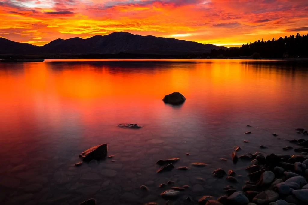 Lake Tekapo at sunrise with orange sky and clouds.