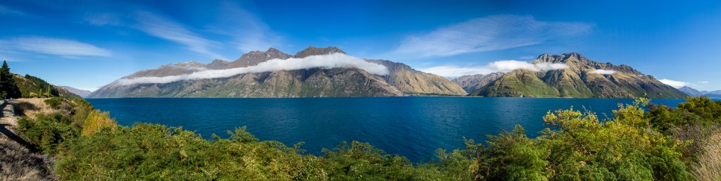 A long white cloud hangs over a New Zealand lake in this panorama.