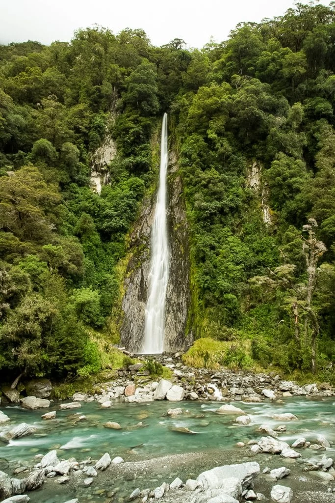Thunder Creek Falls near Haast, New Zealand is a long, narrow waterfall into a river.