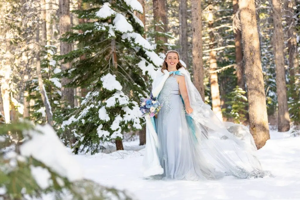 An April Elopement bride in the forest of Northern California with a cloak after snowfall.