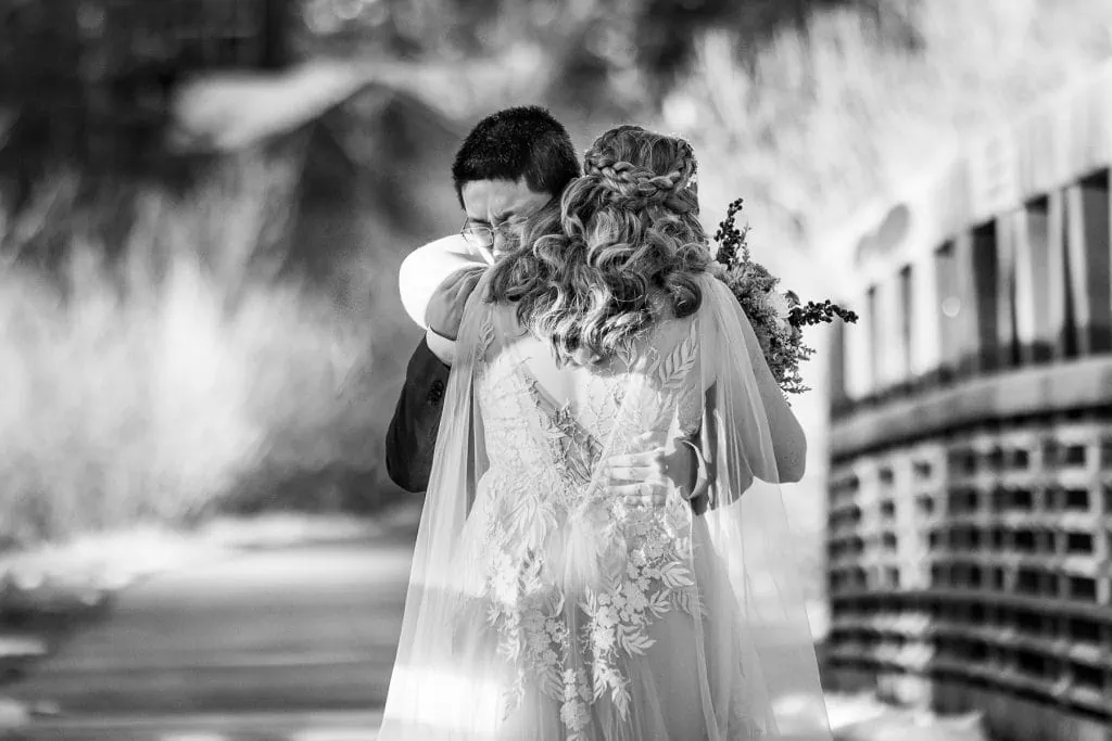A black and white of a groom embracing his bride while crying.