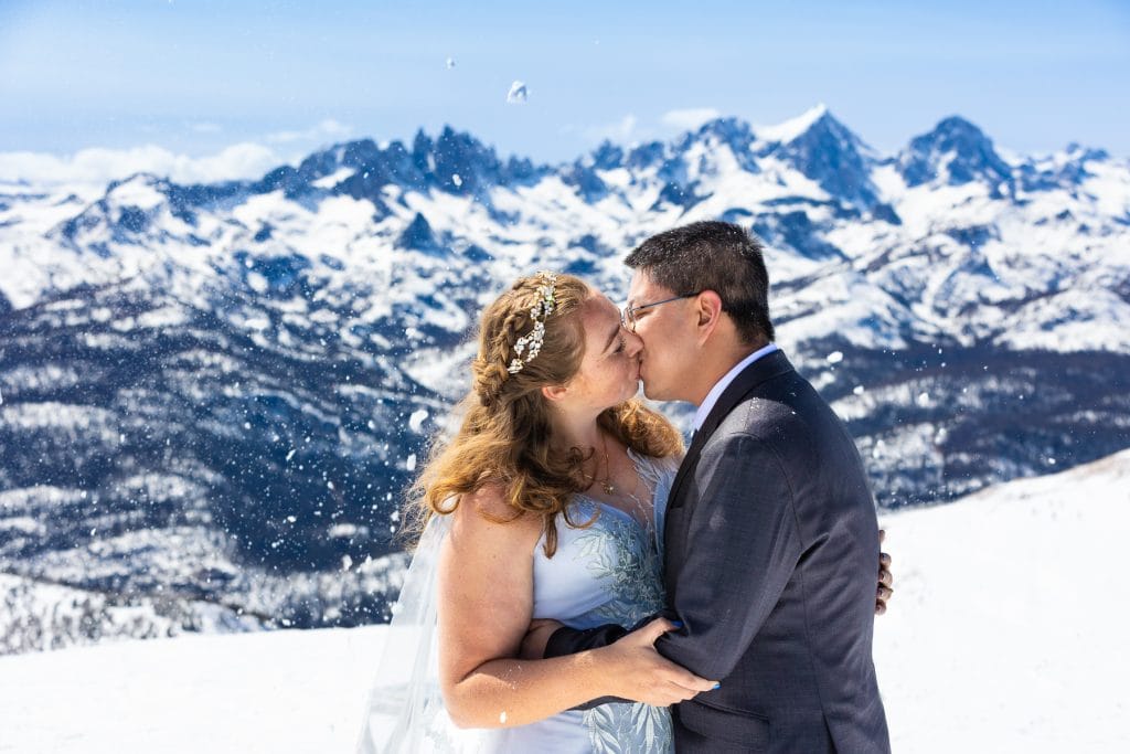 Snow falls around a wedding couple as they smooth in front of the Minaret mountains in California.