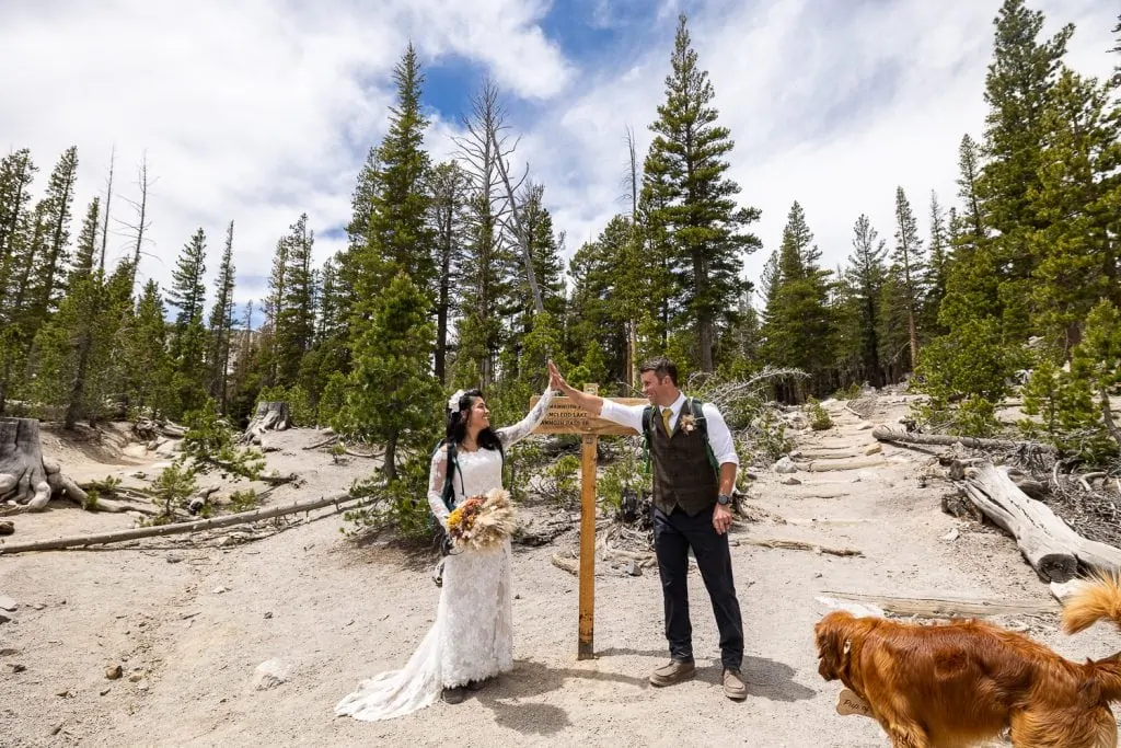 An elopement couple high-fives each other at a trailhead in Yosemite National Park.