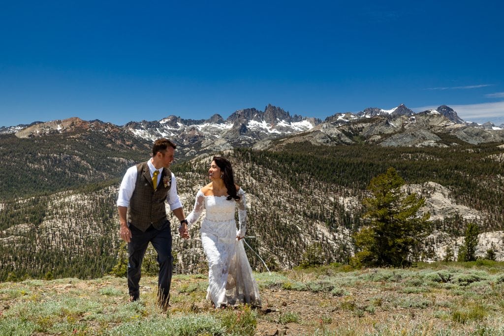 A california mountain elopement location in Mammoth lakes with Minaret vista in the background as a wedding couple walks hand in hand towards the camera.