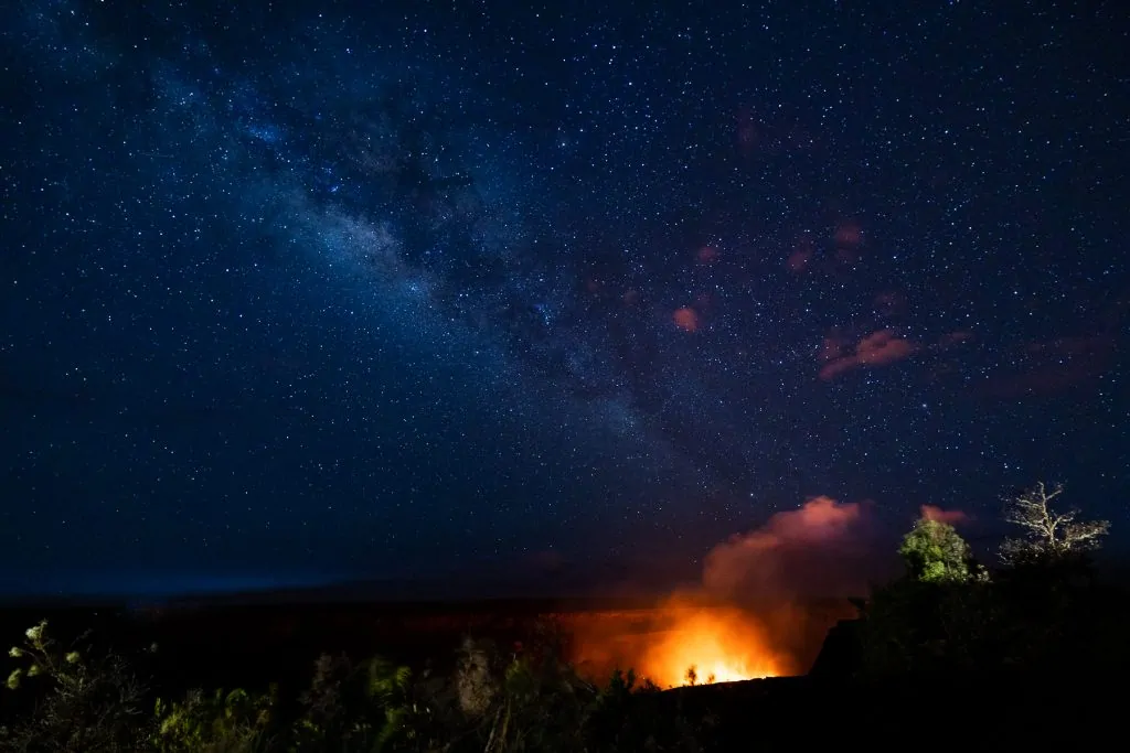 A unique photo of the milky way stretching over Hawaii volcanoes national park mid eruption.