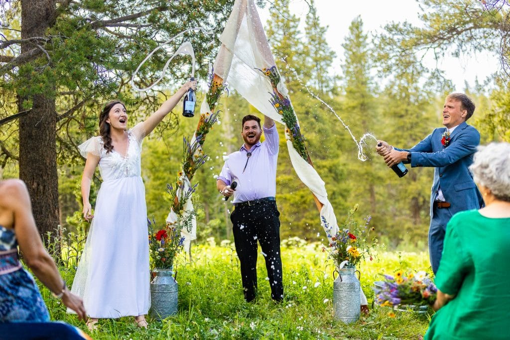 A wedding couple sprays champagne during their wedding ceremony outdoors.