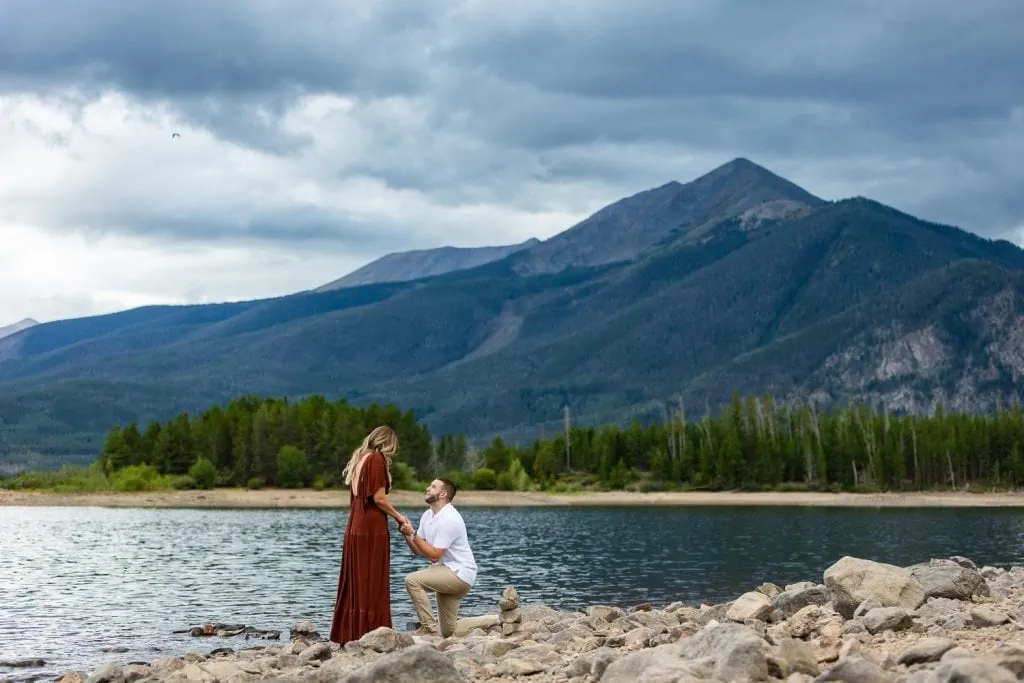 A men goes down on one knee to propose in breckenridge at Lake Dillon.