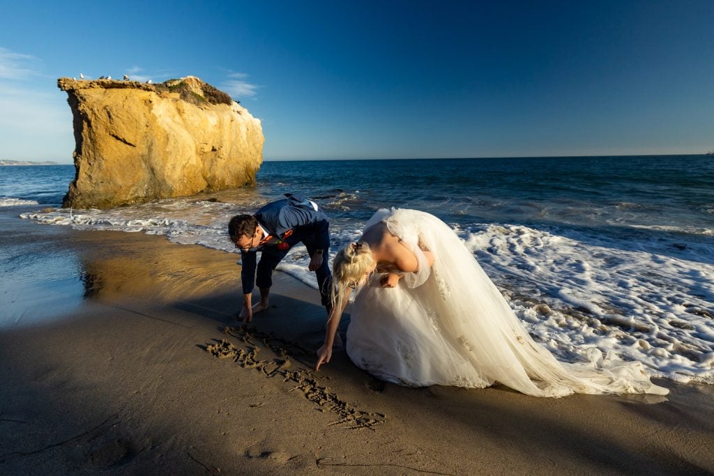 A bride and groom write their last name in the sand after eloping on the beach in Malibu.